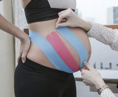 Eine schwangere Frau lässt sich den Bauch tapen